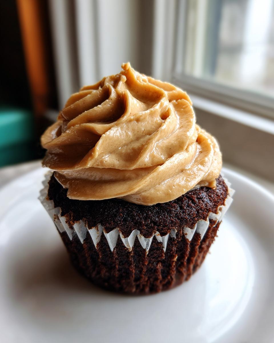 A single decadent chocolate peanut butter cupcakes with a tall swirl of peanut butter frosting on a white plate.