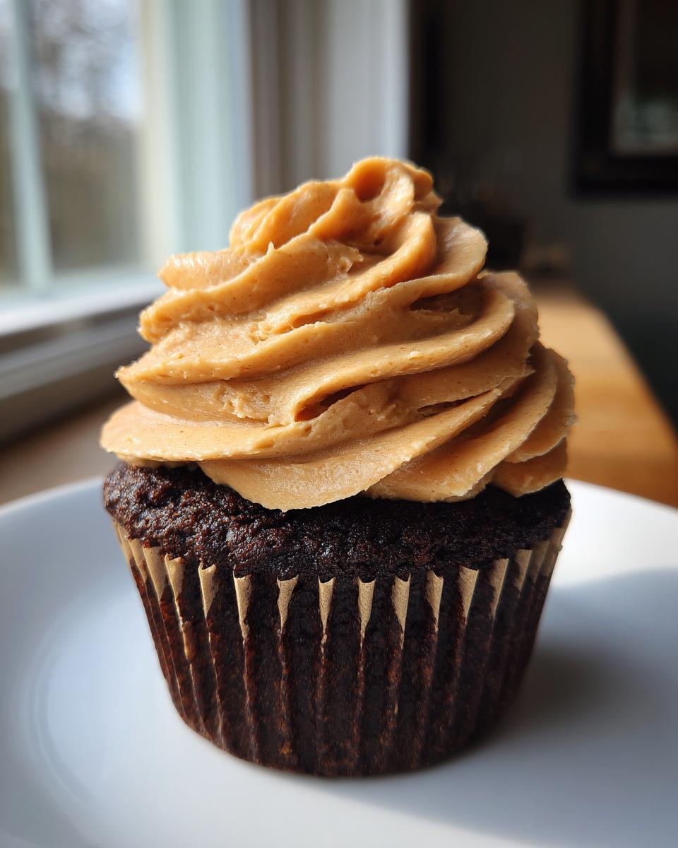 A single, rich chocolate peanut butter cupcakes topped with a tall swirl of peanut butter frosting, sitting on a white plate.