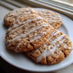 Close-up of three soft Cinnamon Toast Crunch cookies drizzled with white vanilla glaze on a white plate.