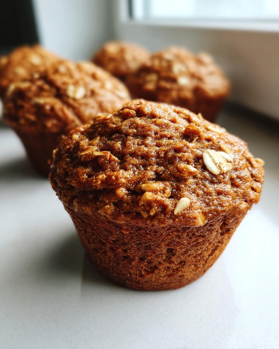 A close-up of a freshly baked banana oatmeal muffin topped with visible rolled oats.