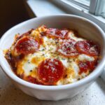 Close-up of a baked cottage cheese pizza bowl topped with melted mozzarella, spicy pepperoni slices, and dried herbs.