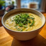 A close-up of a bowl of creamy, yellow chickpea soup garnished heavily with chopped fresh parsley.