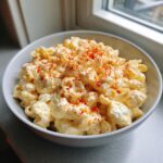 A close-up of creamy deviled egg pasta salad tossed with elbow macaroni and sprinkled generously with paprika.