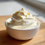 A close-up of perfectly piped, creamy garlic aioli swirled high in a small white bowl.