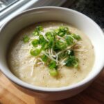A close-up of a bowl of creamy low calorie potato soup topped with shredded cheese and fresh green onions.