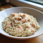 A close-up of creamy salmon lemon risotto topped with flaked salmon and fresh dill in a white bowl.