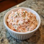 A close-up of creamy, pink smoked salmon dip topped with fresh dill in a white bowl.