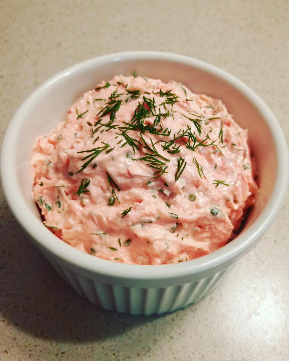 A close-up view of creamy, pink smoked salmon dip topped generously with fresh dill in a white ramekin.