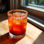 A vibrant, deep red Devils Margarita cocktail served over ice with a spicy chili salt rim.