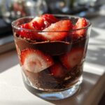 Close-up of a layered dubai chocolate strawberry cup dessert in a clear glass with fresh strawberry slices.