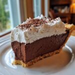 A tall, decadent slice of french silk pie featuring a thick chocolate filling, topped with whipped cream and chocolate shavings.