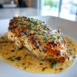 Close-up of a golden-brown garlic parmesan chicken breast covered in creamy sauce and fresh parsley.