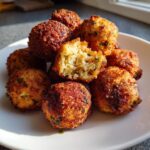A pile of golden brown, crispy stuffing balls on a white plate, with one broken open showing the soft interior.