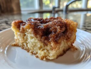 Close-up of a warm slice of snickerdoodle cobbler with a gooey cinnamon-sugar topping on a white plate.