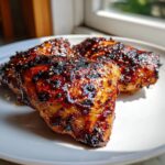Three pieces of sticky, caramelized hawaiian huli huli chicken, sprinkled with sesame seeds, resting on a white plate.