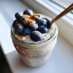 Close-up of a jar of creamy chia pudding topped with fresh blueberries and a sprinkle of cinnamon.