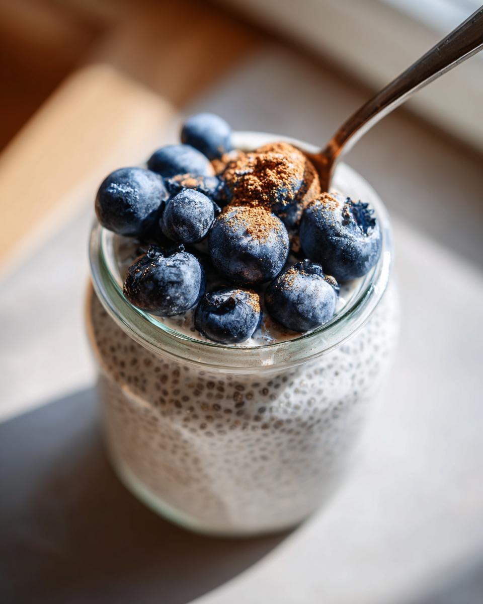 Close-up of a jar filled with creamy chia pudding topped with fresh blueberries and a sprinkle of cinnamon.
