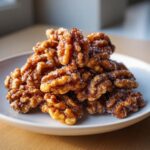 A pile of glistening, sugar-coated candied walnuts served on a light gray plate.