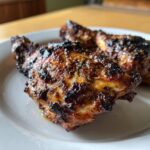 Close-up of juicy, charred pieces of Jamaican Jerk Chicken resting on a white plate.