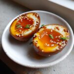 Two halves of a perfectly cooked, brown-stained marinated eggs with jammy yolks, topped with sesame seeds and chives.