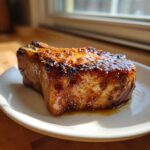 A thick, juicy pork chop with a caramelized, mustard-seed glaze resting on a white plate.