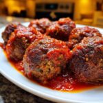 A close-up shot of several rich, browned italian meatballs generously coated in bright red tomato sauce on a white plate.