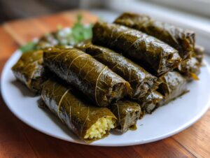 A close-up of a stack of glistening lemony rice-stuffed grape leaves on a white plate.