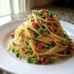 A beautifully plated mound of light pasta with pancetta & peas, garnished with fresh parsley.
