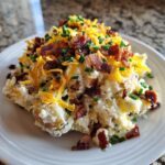 A generous serving of loaded baked potato salad topped with shredded cheddar cheese, bacon bits, and fresh chives.
