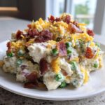 A mound of creamy pea salad mixed with potatoes, topped generously with shredded cheddar cheese and crispy bacon pieces.