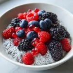 A white bowl filled with creamy low calorie chia pudding snack topped generously with fresh raspberries, blueberries, and blackberries.