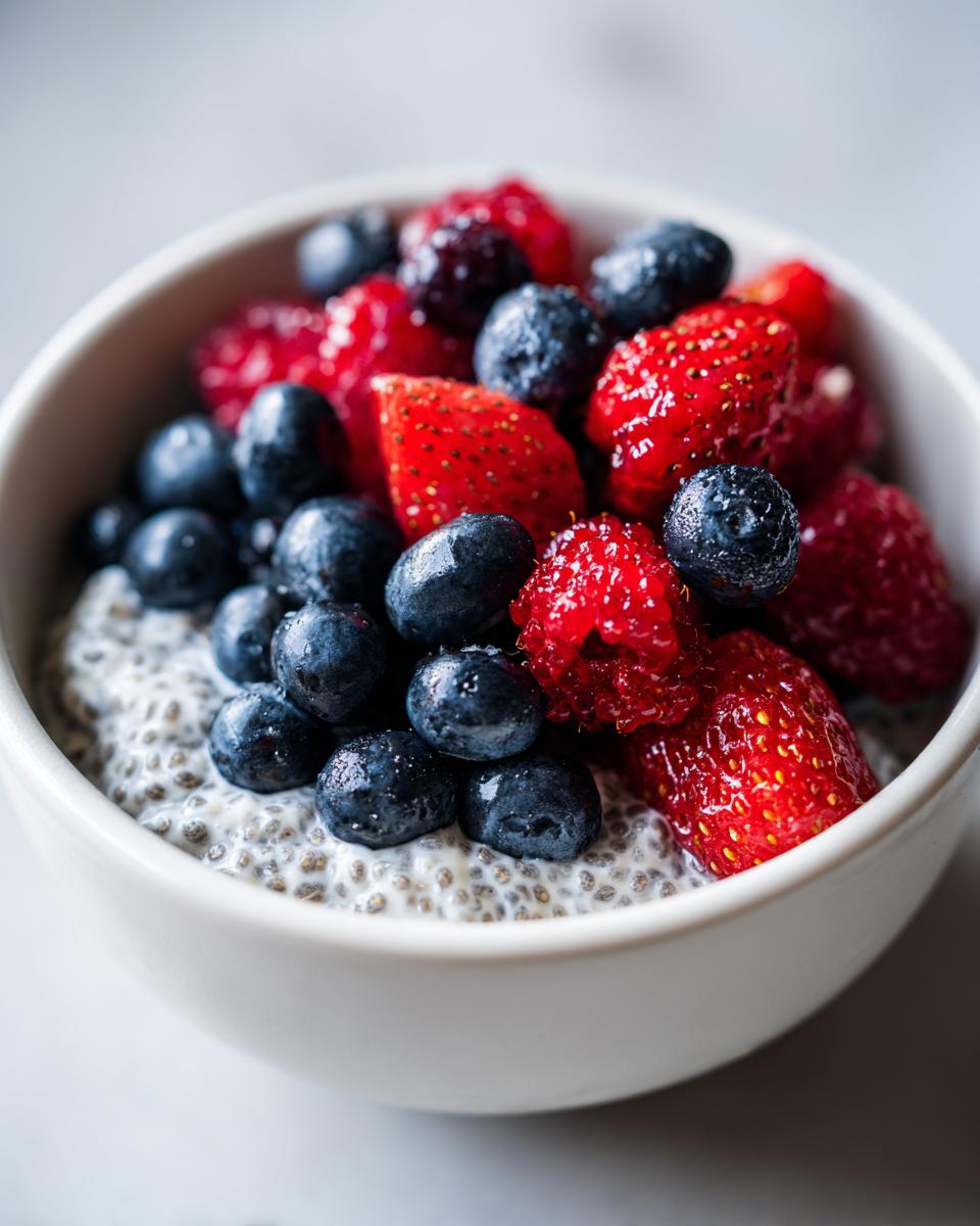 Close-up of a white bowl filled with low calorie chia pudding snack topped generously with fresh blueberries, strawberries, and raspberries.