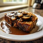 A close-up of a thick slice of meatloaf with mushroom gravy generously poured over the top.