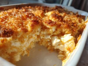 Close-up of a creamy million dollar chicken casserole with a deeply browned, crunchy topping in a white baking dish.