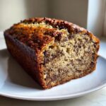 A close-up cross-section of a moist chocolate chip banana bread loaf on a white plate.