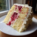 A moist slice of white chocolate raspberry cake with white frosting and visible raspberry filling.