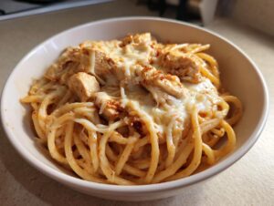 A close-up view of a serving of one pot chicken parm pasta topped with melted mozzarella cheese and chunks of seasoned chicken.