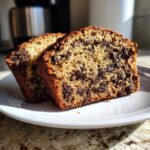 Two thick slices of moist, chocolate-studded oreo banana bread resting on a white plate.