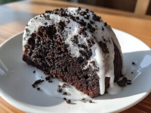 Close-up of a moist slice of dark chocolate Oreo bundt cake topped with white glaze and cookie crumbs.