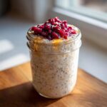 A glass jar filled with overnight chia seed pudding with yogurt, topped with bright red berries and a drizzle of honey.