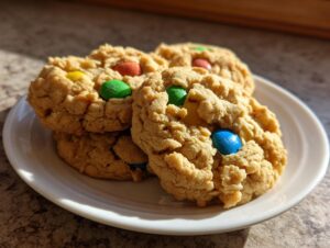 A stack of three textured peanut butter m&m cookies featuring colorful candy pieces, served on a small white plate.