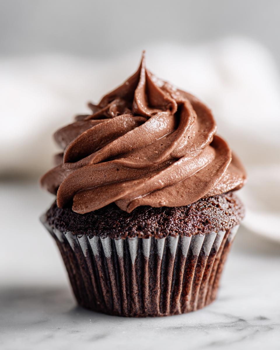 A close-up of a rich chocolate cupcake topped with a tall swirl of dark chocolate frosting.