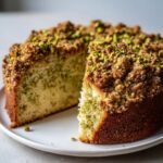 A slice cut from a moist pistachio coffee cake topped with brown sugar crumble and chopped pistachios.