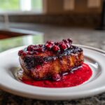 A perfectly cooked pork chop covered in a thick, dark raspberry balsamic glaze and topped with fresh raspberries.