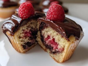 Close-up of a raspberry chocolate cupcakes cut in half, showing the moist cake, raspberry filling, and chocolate ganache topping.