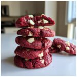 A stack of four chewy red velvet cake mix cookies, studded with white chocolate chips, with the top cookie broken open.