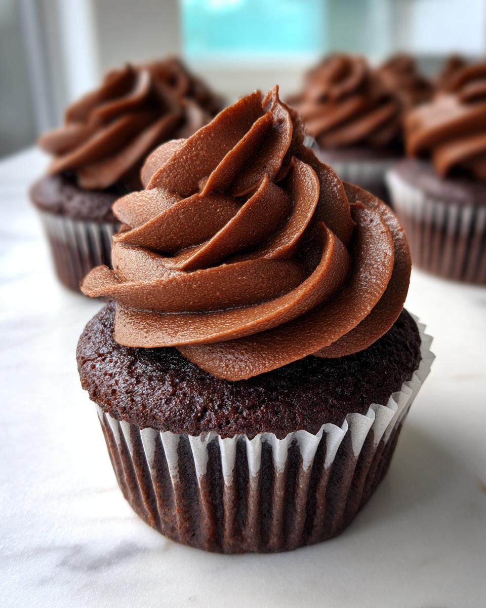 Close-up of a rich, dark chocolate cupcake topped with a high swirl of smooth chocolate frosting.