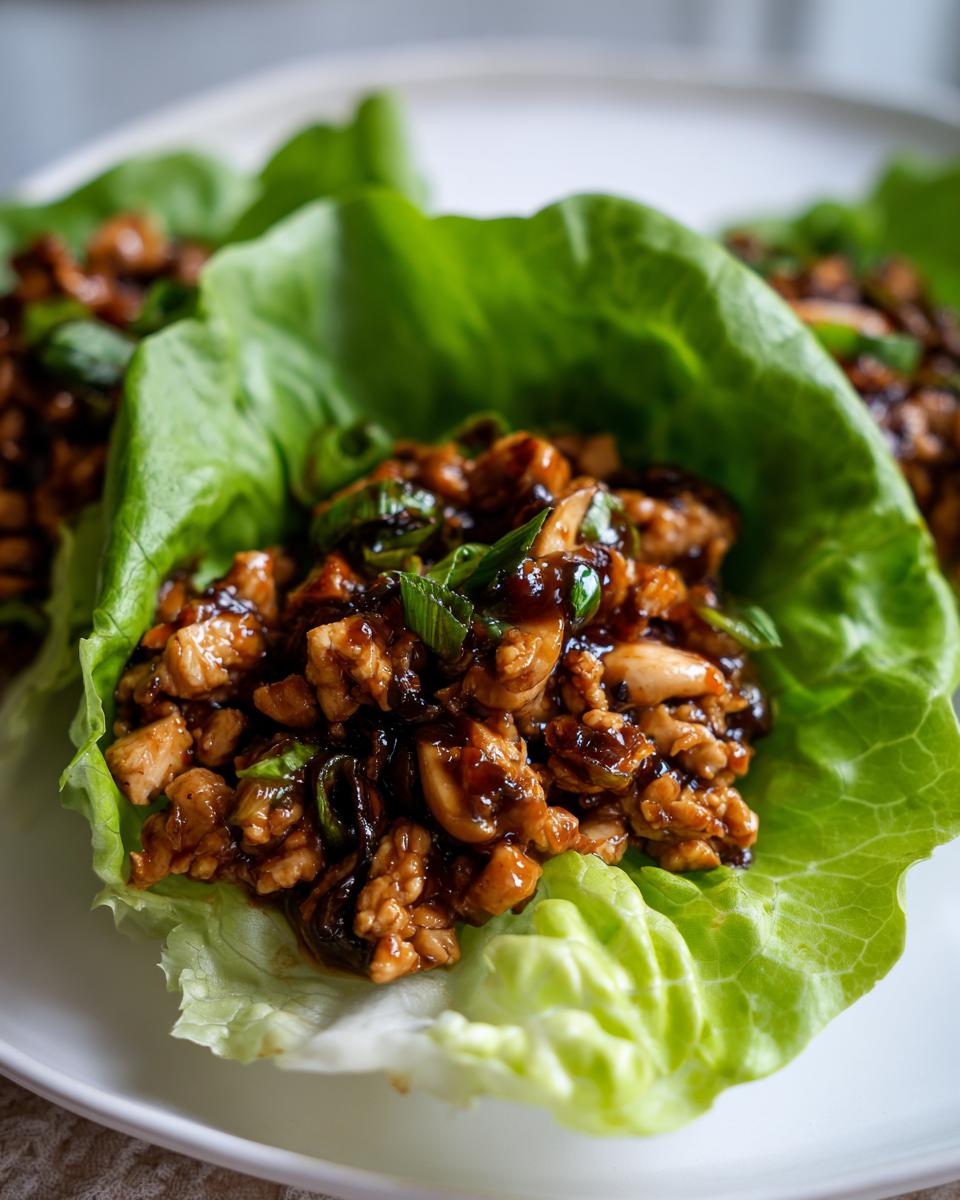 Close-up of a fresh lettuce cup filled with saucy, savory chicken lettuce wraps mixture and green onions.