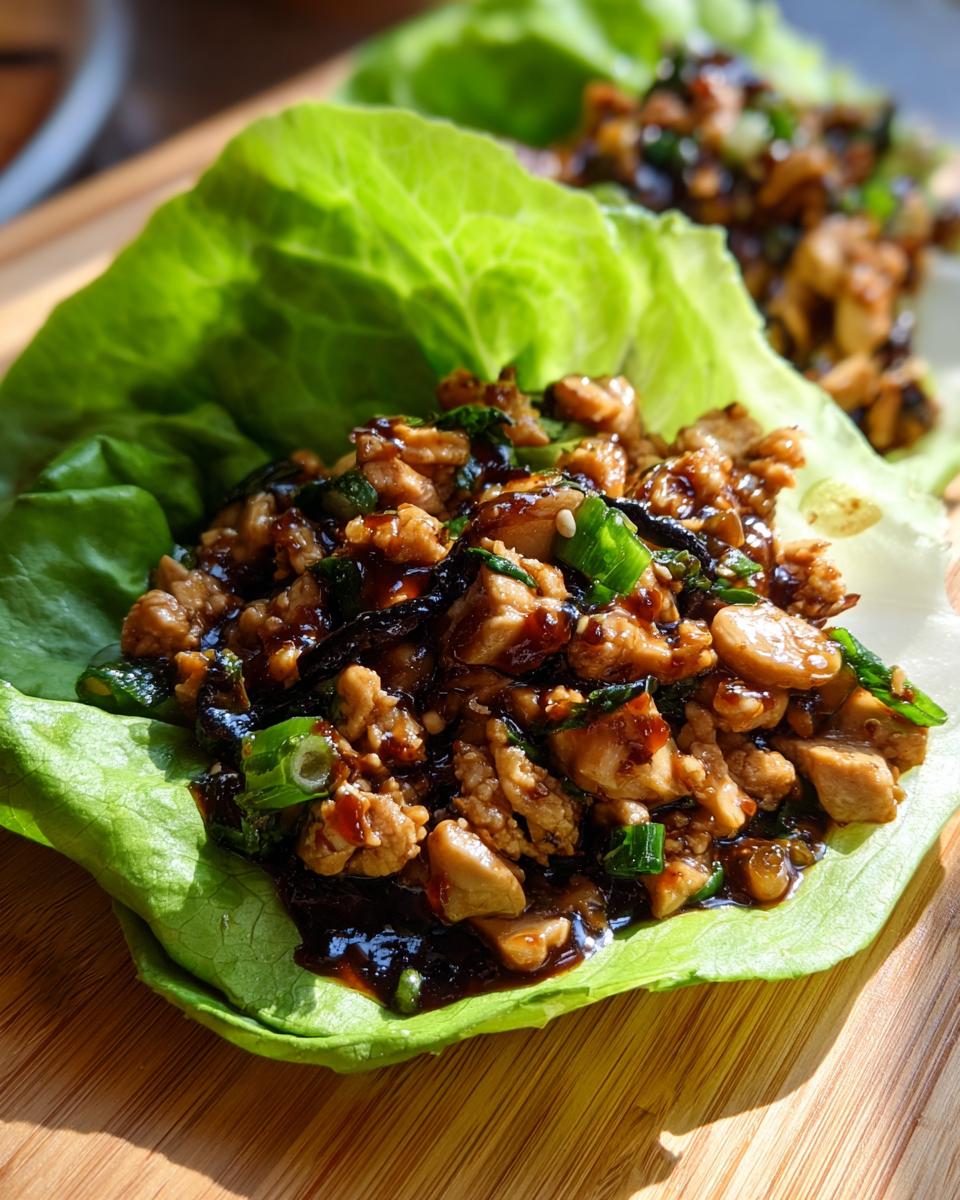 A close-up of a fresh lettuce cup filled with saucy, ground chicken lettuce wraps mixture, garnished with green onions.