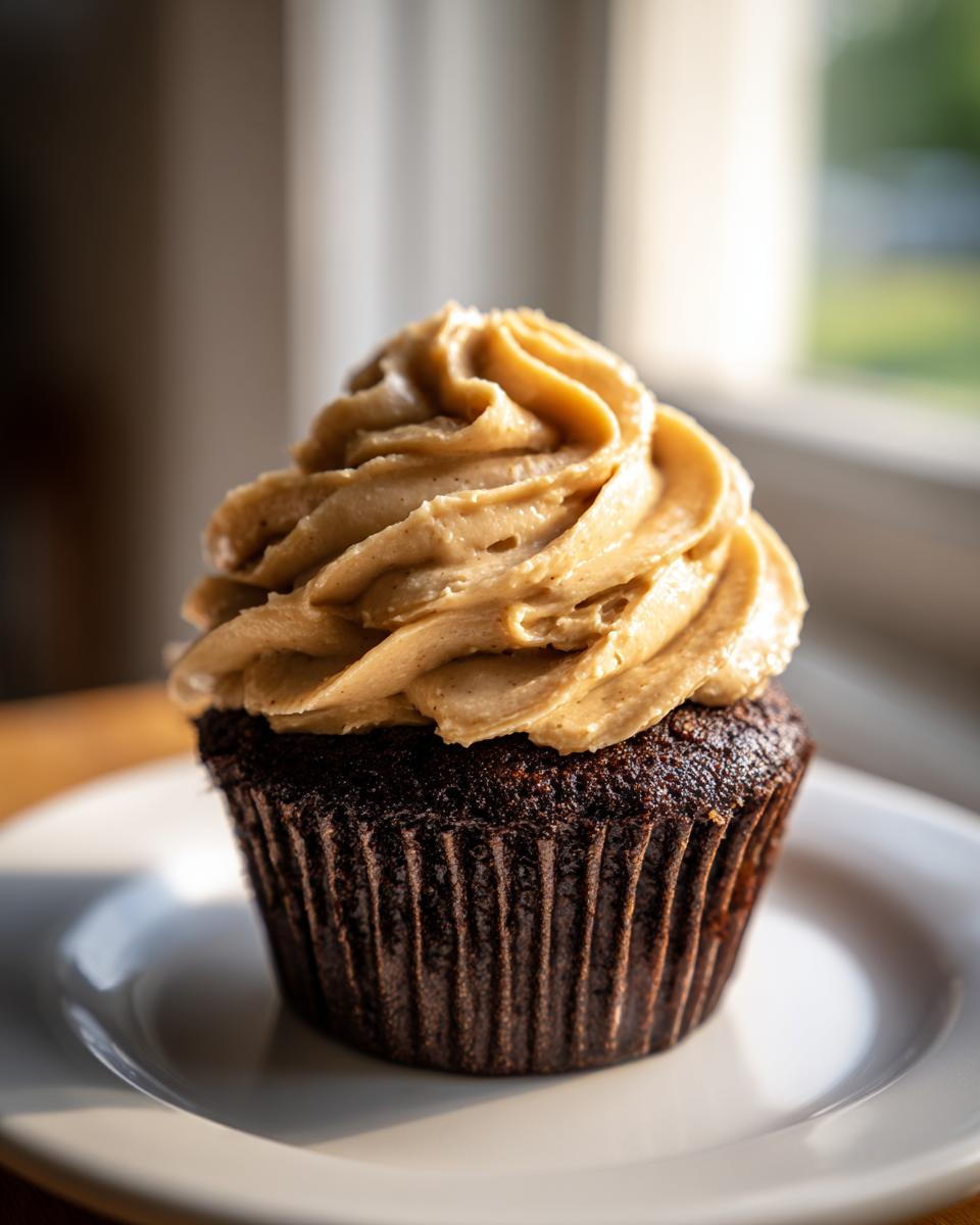 A single, rich chocolate cupcake topped with a tall swirl of peanut butter frosting, sitting on a white plate.